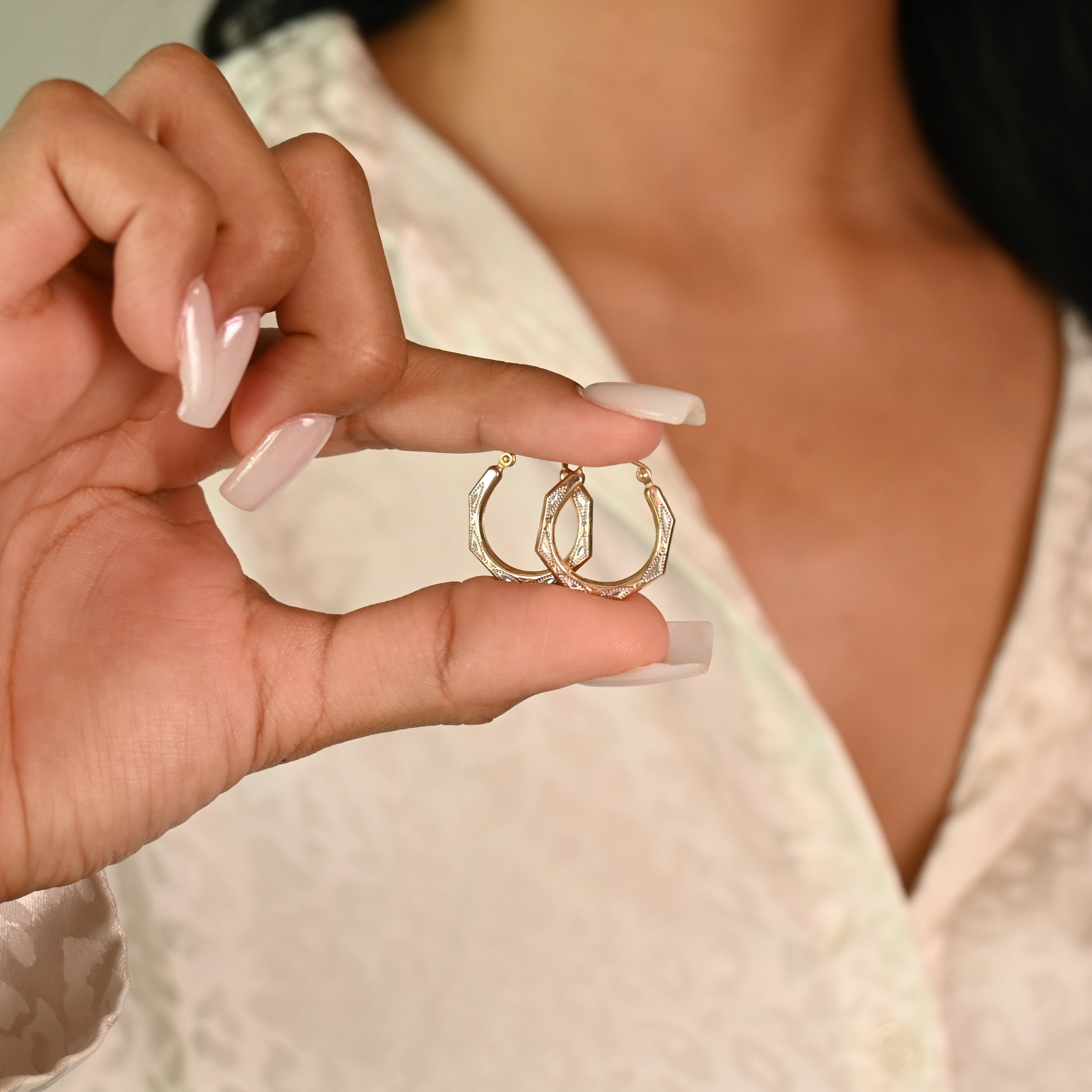 Hand holding two gold hoop earrings with a blurred background