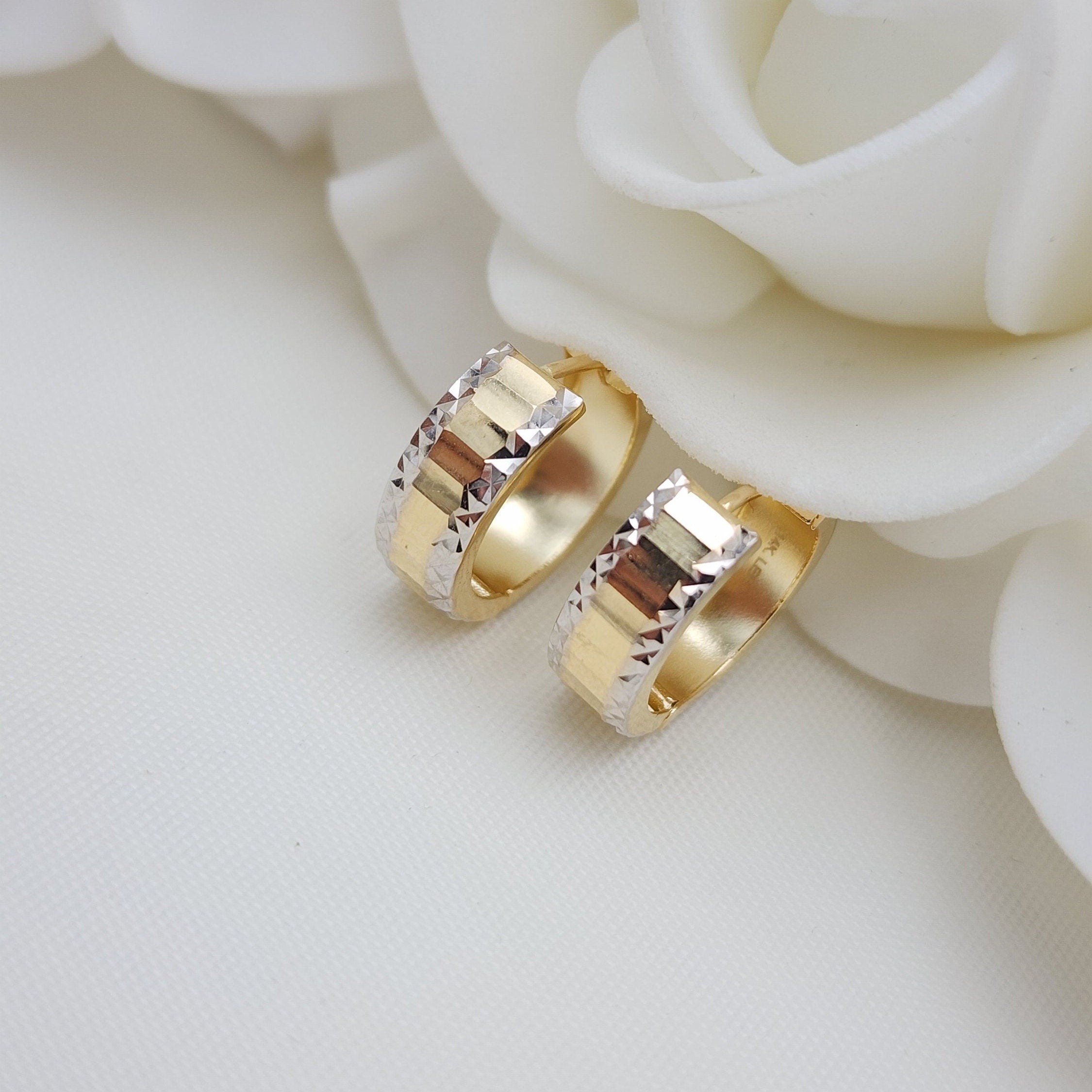 May include: Two gold hoop earrings with a diamond-shaped pattern. The earrings are made of two-toned gold, with a yellow gold band and a white gold trim.