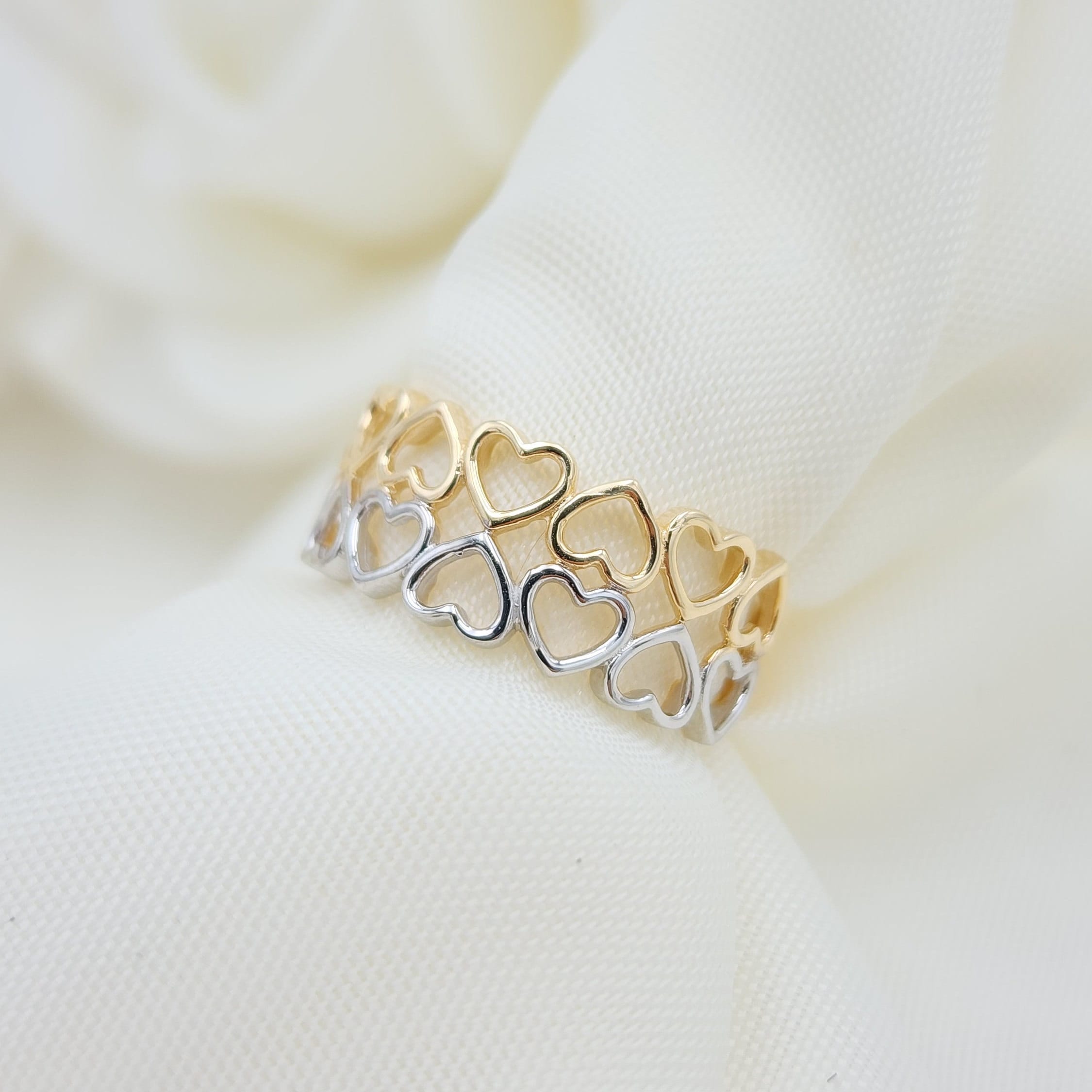 May include: A gold and silver ring with a heart design. The ring is made of two rows of interlocking hearts, with the top row being gold and the bottom row being silver.
