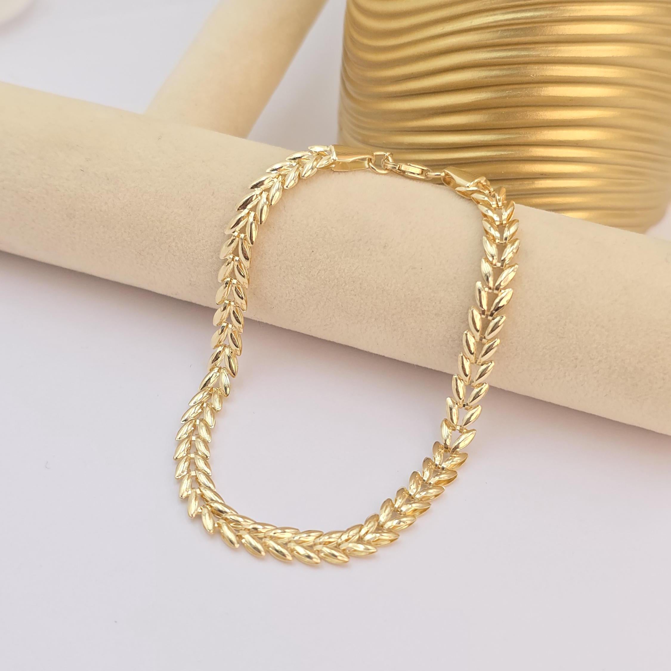 May include: A gold chain bracelet with a wheat chain design. The bracelet is on a light brown surface.