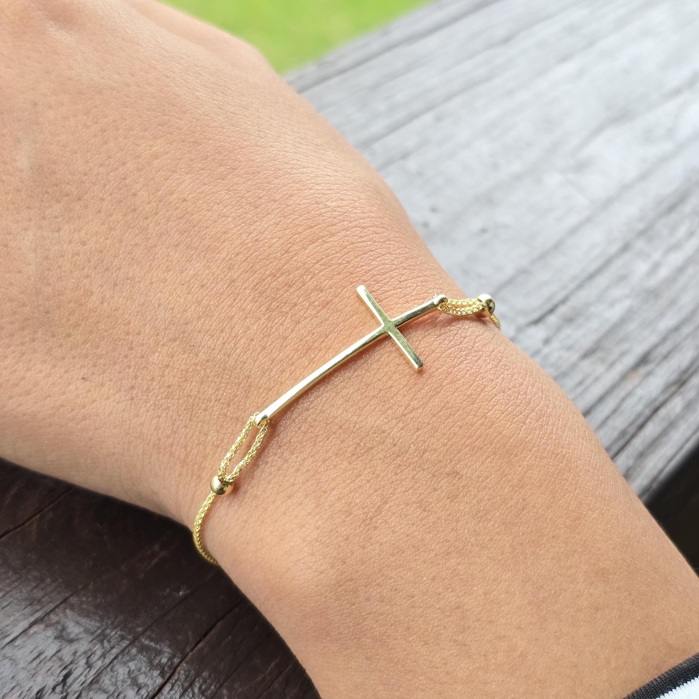 May include: Gold cross bracelet with adjustable sliding knots. The minimalist cross pendant is attached to delicate gold-tone cords.  The bracelet features small gold beads at each end of the cords.  This simple, elegant bracelet is perfect for everyday wear.