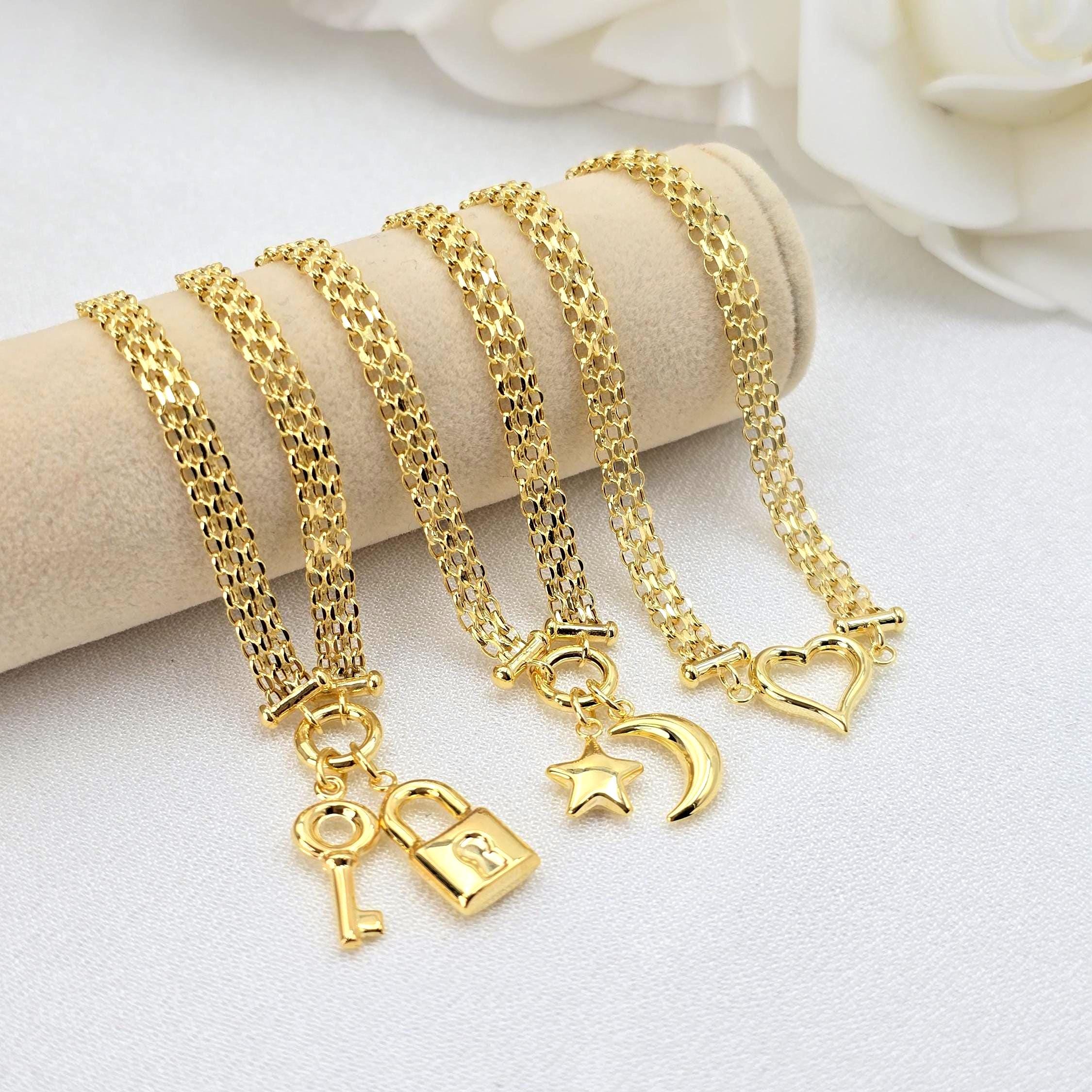 May include: Four gold chain bracelets with different charms.  Each bracelet features a delicate, layered chain design and a unique pendant: a padlock and key, a star, a crescent moon, and a heart. The charms are intricately detailed and add a touch of elegance to the simple chain design. The bracelets are displayed on a beige surface.