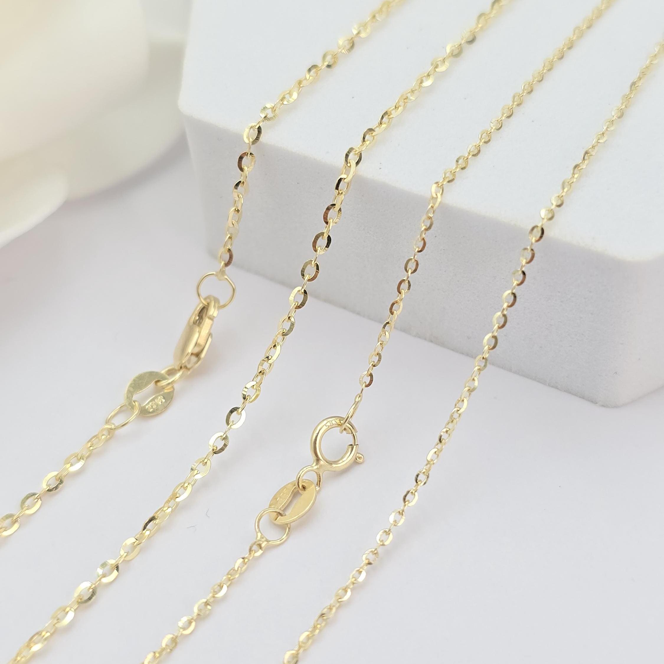 May include: Three gold chains of different lengths on a white surface. The chains are made of small, oval-shaped links. The chains have a lobster clasp closure.