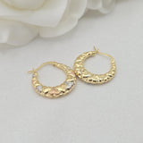 May include: Close-up of a pair of gold hoop earrings. The hoops are adorned with small, heart-shaped details in three-toned gold: yellow, white, and rose. The earrings have a smooth, curved design and are displayed against a white background.